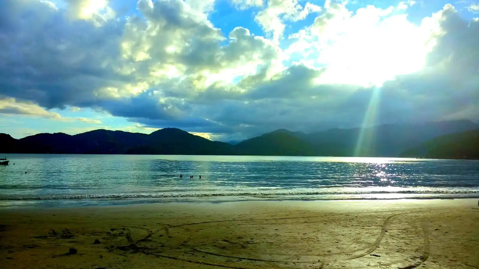 Sol atravessando as nuvens sobre o mar calmo do Lázaro, com a serra ao fundo